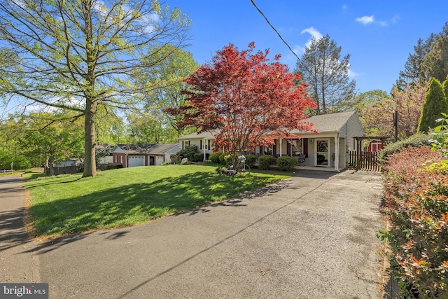 view of property hidden behind natural elements featuring fence, a garage, driveway, and a front lawn