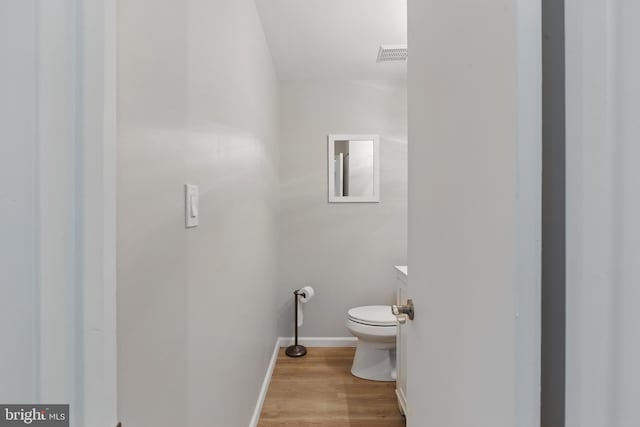 half bathroom with visible vents, wood finished floors, baseboards, vanity, and toilet