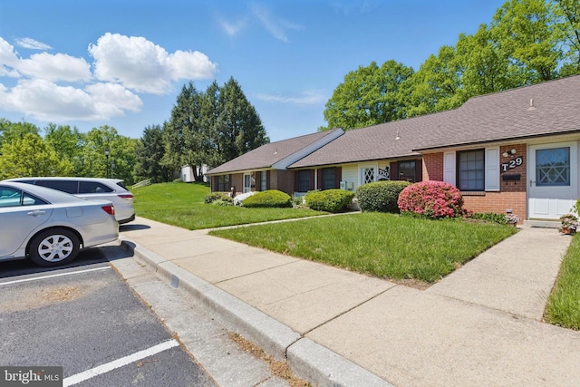 view of front of house featuring brick siding, uncovered parking, a shingled roof, and a front lawn