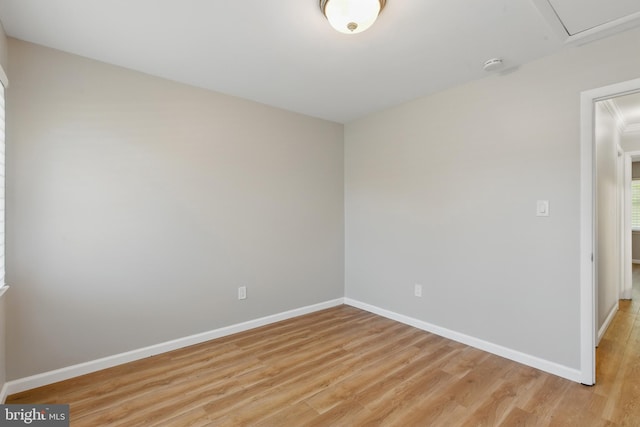 empty room featuring light wood-style floors, baseboards, and attic access