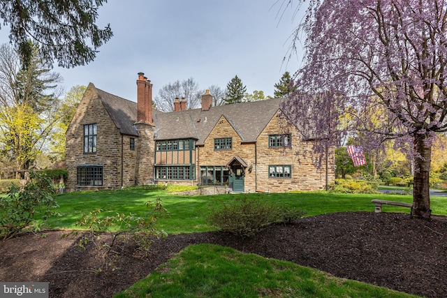 rear view of property featuring a lawn, a chimney, and stone siding