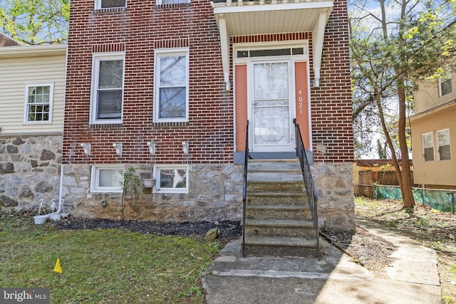view of exterior entry with fence and brick siding