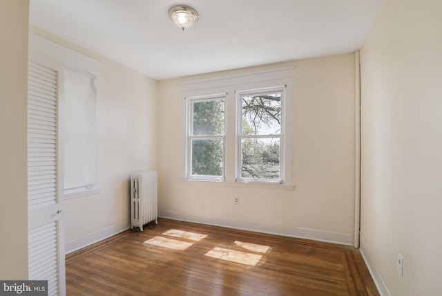 empty room featuring wood finished floors, baseboards, and radiator heating unit