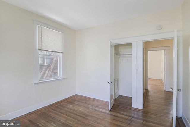 unfurnished bedroom with baseboards, a closet, and dark wood-type flooring