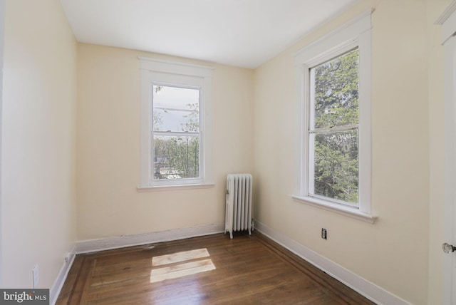 spare room with baseboards, radiator, and wood finished floors