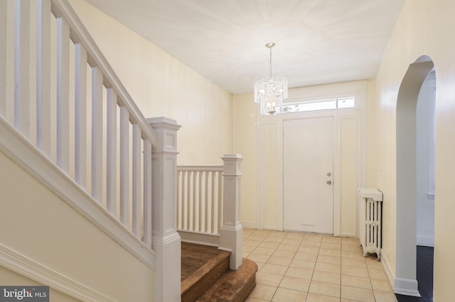foyer entrance with arched walkways, stairs, light tile patterned floors, and a chandelier