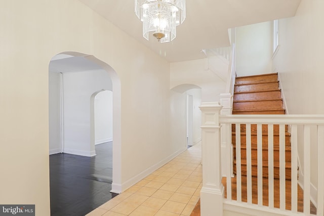 corridor featuring arched walkways, stairway, a chandelier, and tile patterned flooring