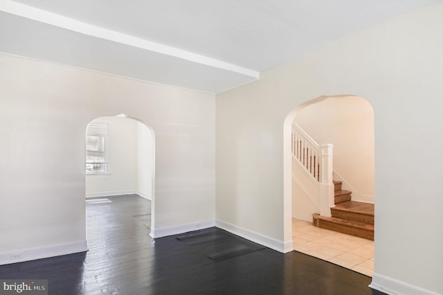 empty room featuring arched walkways, baseboards, wood finished floors, and stairway