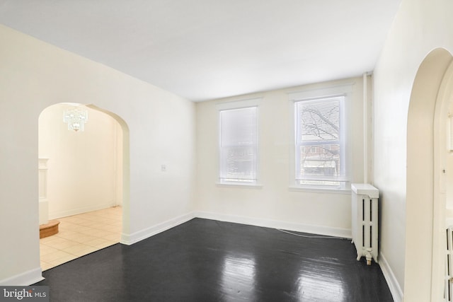 unfurnished room with radiator heating unit, arched walkways, baseboards, and dark wood-style floors