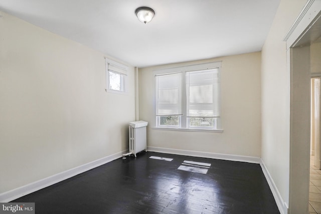 spare room with baseboards, radiator, and wood finished floors