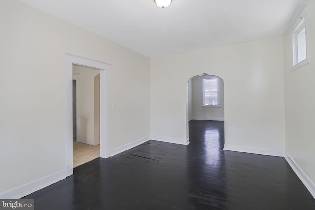spare room featuring arched walkways, baseboards, and wood finished floors