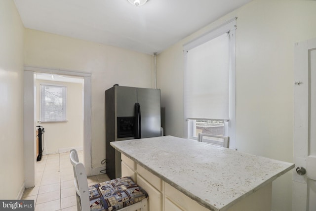 kitchen with stainless steel fridge, light tile patterned floors, a center island, and light stone countertops