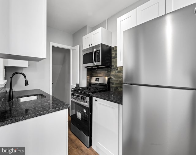 kitchen with wood finished floors, stainless steel appliances, backsplash, a sink, and white cabinetry