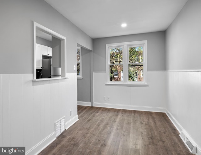 unfurnished room featuring a wainscoted wall, visible vents, and dark wood finished floors