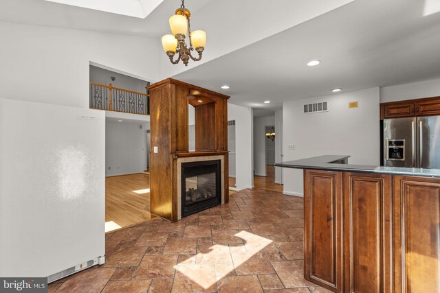 kitchen with stainless steel refrigerator with ice dispenser, visible vents, dark countertops, a notable chandelier, and stone tile floors