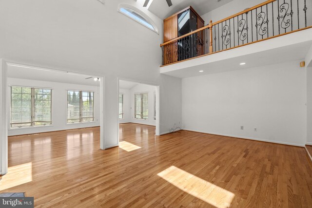 unfurnished living room featuring a ceiling fan, baseboards, wood finished floors, and a high ceiling