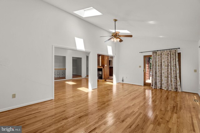 unfurnished living room with a fireplace, light wood-style floors, baseboards, a ceiling fan, and a skylight