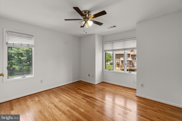empty room with baseboards, visible vents, a healthy amount of sunlight, and wood finished floors