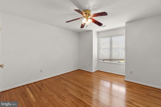 empty room with a ceiling fan, baseboards, visible vents, and wood finished floors