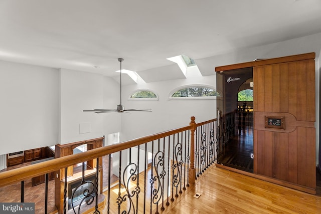 hall featuring light wood finished floors, an upstairs landing, and a skylight