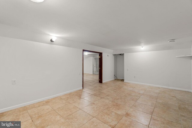 finished below grade area featuring light tile patterned flooring and baseboards