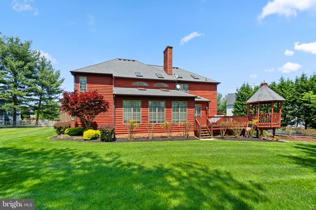 back of property featuring a lawn, a deck, a chimney, a shingled roof, and a gazebo