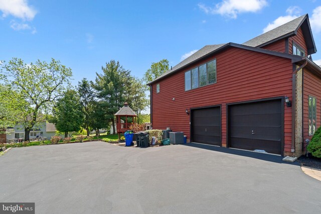 view of property exterior with an attached garage, central AC unit, and aphalt driveway