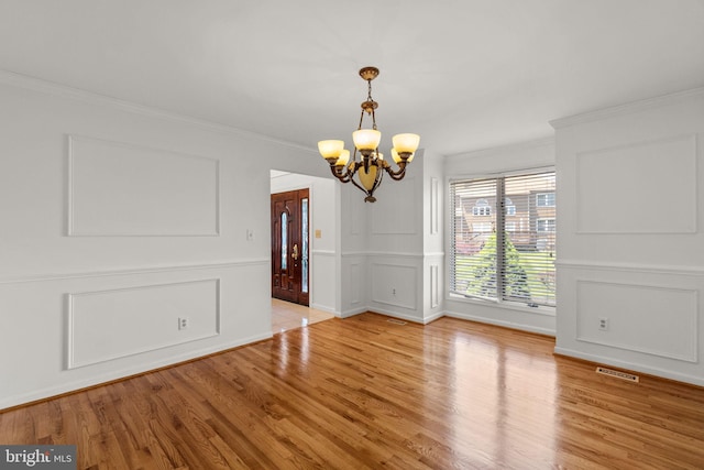 unfurnished dining area with visible vents, ornamental molding, a decorative wall, wood finished floors, and a chandelier