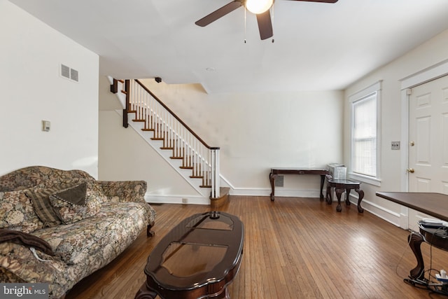 living area featuring stairway, visible vents, ceiling fan, hardwood / wood-style floors, and baseboards
