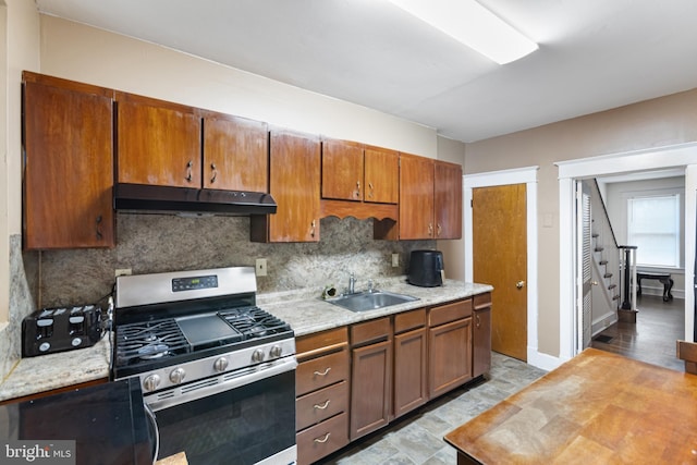 kitchen featuring decorative backsplash, stainless steel gas range oven, under cabinet range hood, light countertops, and a sink