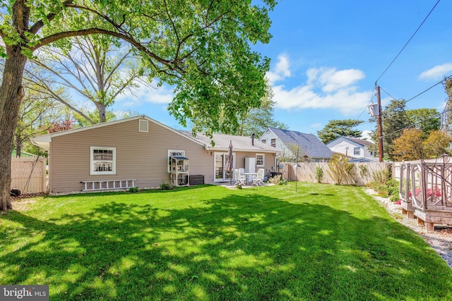rear view of house with a fenced backyard, a yard, and central AC