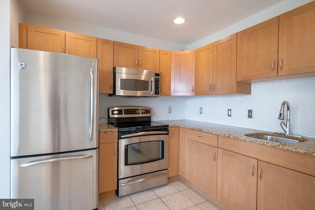kitchen featuring light stone counters, light tile patterned floors, decorative backsplash, a sink, and appliances with stainless steel finishes