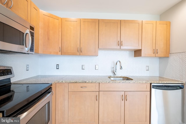kitchen with a sink, light brown cabinets, light stone counters, backsplash, and appliances with stainless steel finishes