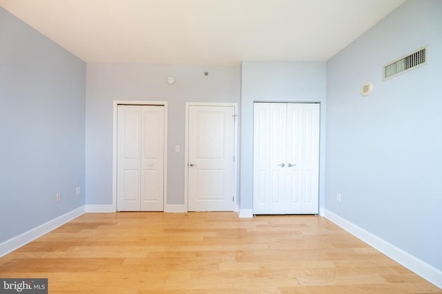 unfurnished bedroom featuring visible vents, two closets, light wood-style flooring, and baseboards