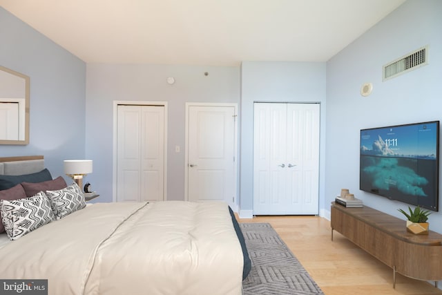 bedroom with light wood finished floors, visible vents, and multiple closets