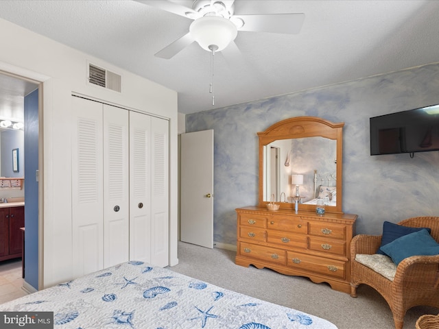 bedroom with ceiling fan, light colored carpet, ensuite bathroom, visible vents, and a closet