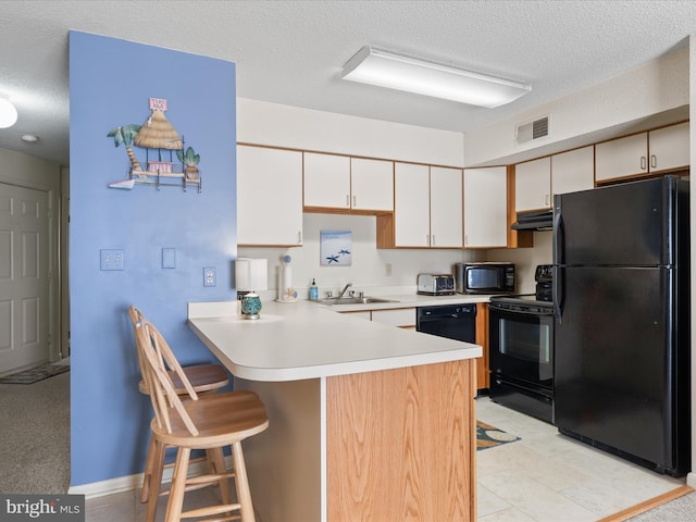 kitchen with a textured ceiling, visible vents, a sink, black appliances, and a peninsula