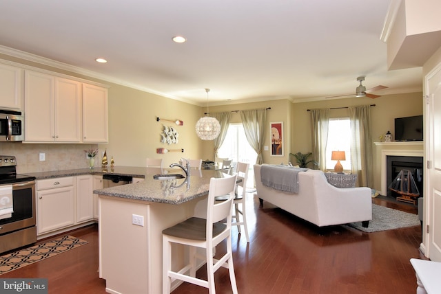kitchen with white cabinets, appliances with stainless steel finishes, dark wood-style floors, and a breakfast bar