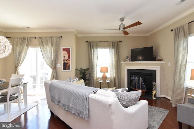 living room featuring dark wood-style flooring, a ceiling fan, a glass covered fireplace, and ornamental molding
