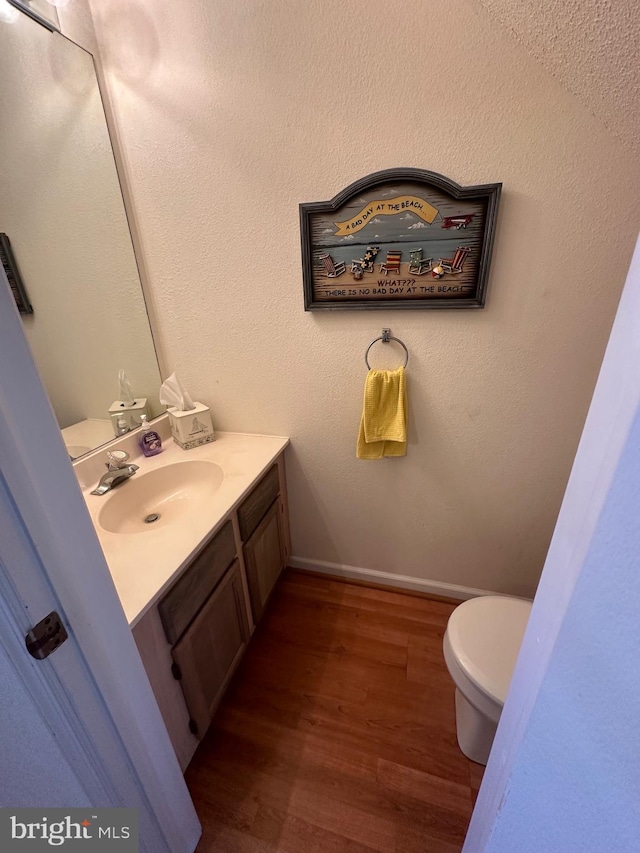 bathroom featuring baseboards, wood finished floors, toilet, and vanity