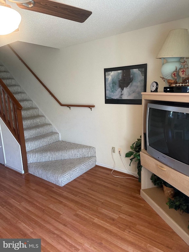 stairway with baseboards, wood finished floors, and a textured ceiling