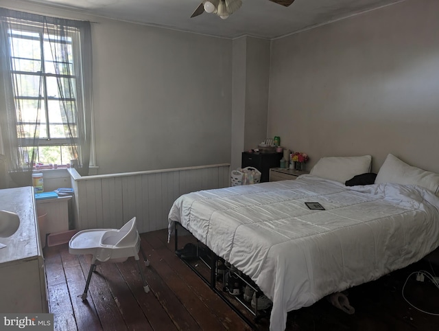 bedroom featuring ceiling fan, multiple windows, hardwood / wood-style floors, and a wainscoted wall