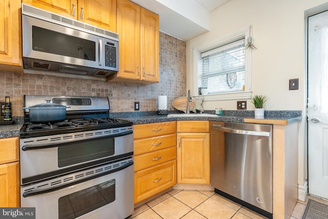 kitchen featuring dark countertops, appliances with stainless steel finishes, a sink, and tasteful backsplash