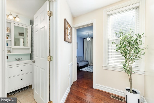 hallway featuring a sink, baseboards, wood finished floors, and visible vents