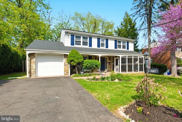 traditional-style home with aphalt driveway, stone siding, covered porch, a front lawn, and a garage