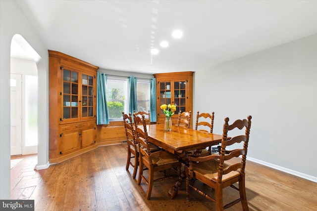 dining space featuring arched walkways, baseboards, and light wood-type flooring
