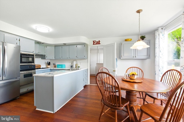 kitchen with appliances with stainless steel finishes, a peninsula, dark wood finished floors, and under cabinet range hood