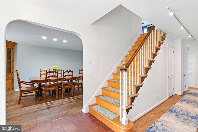 stairs with arched walkways, rail lighting, and baseboards