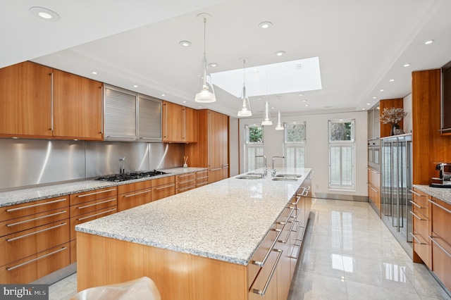 kitchen with a large island, brown cabinets, a skylight, and stainless steel appliances