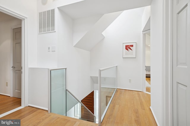 hall with visible vents, baseboards, wood finished floors, and an upstairs landing